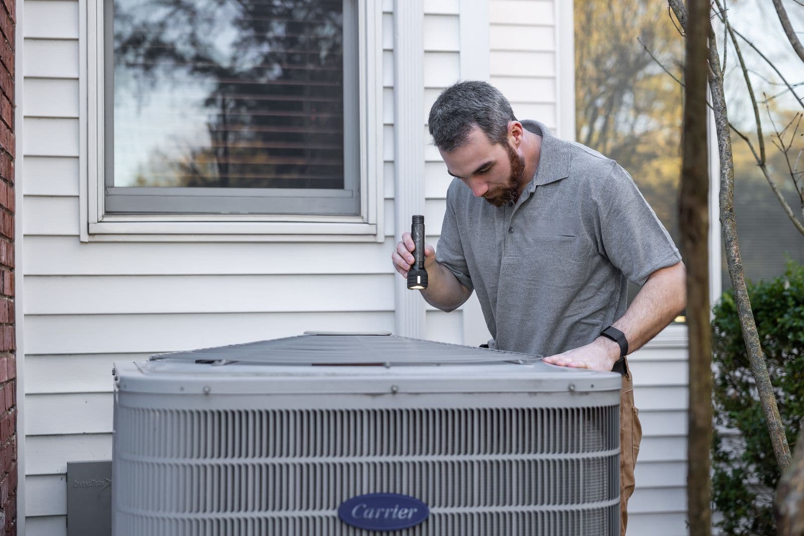 Technician inspecting an outdoor HVAC unit at a home