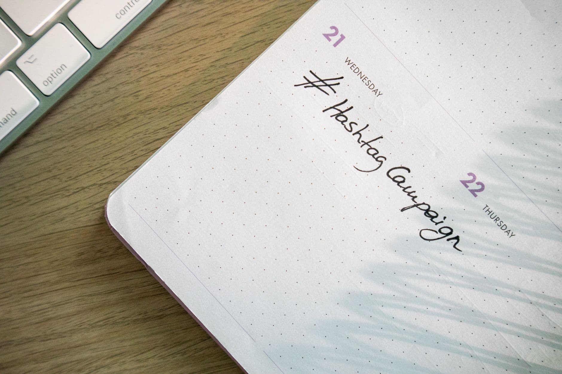 Content planner open to a handwritten hashtag campaign note beside a keyboard