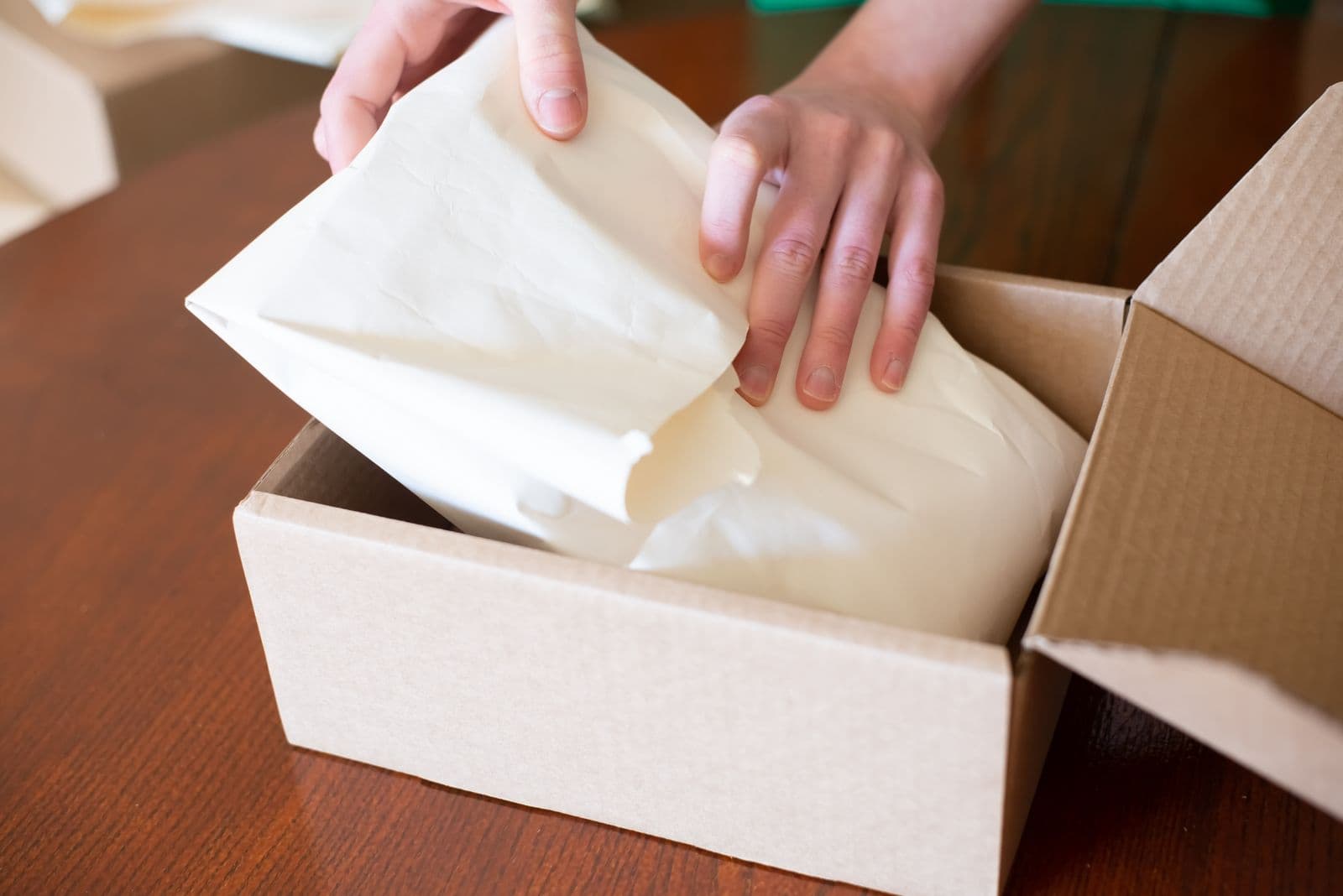 Hands packing a small online order into a cardboard box with white tissue paper