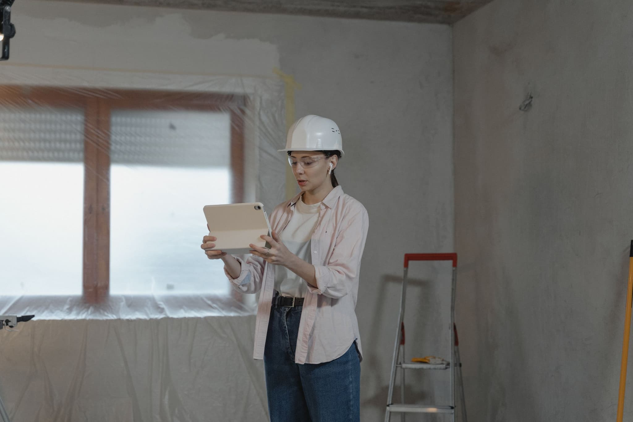 A construction worker in a hard hat reviews a tablet inside an unfinished home