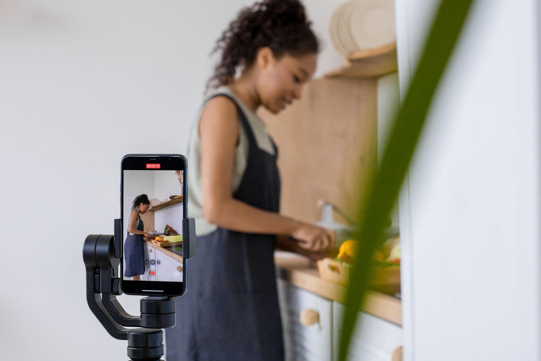 Woman filming a cooking video with a smartphone on a stabilizer in her kitchen