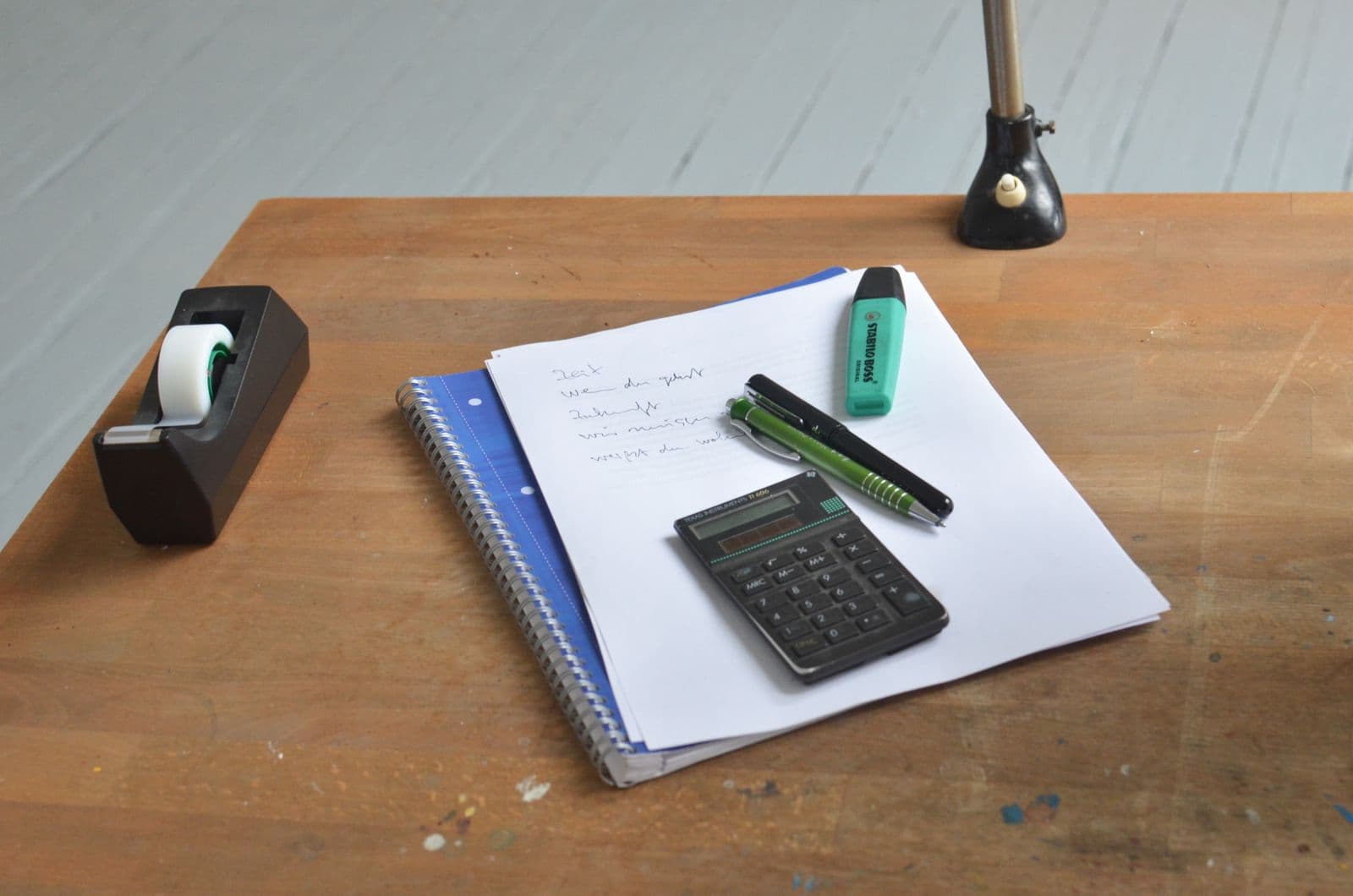 Calculator and planning notes on a wooden desk with pens and a green highlighter